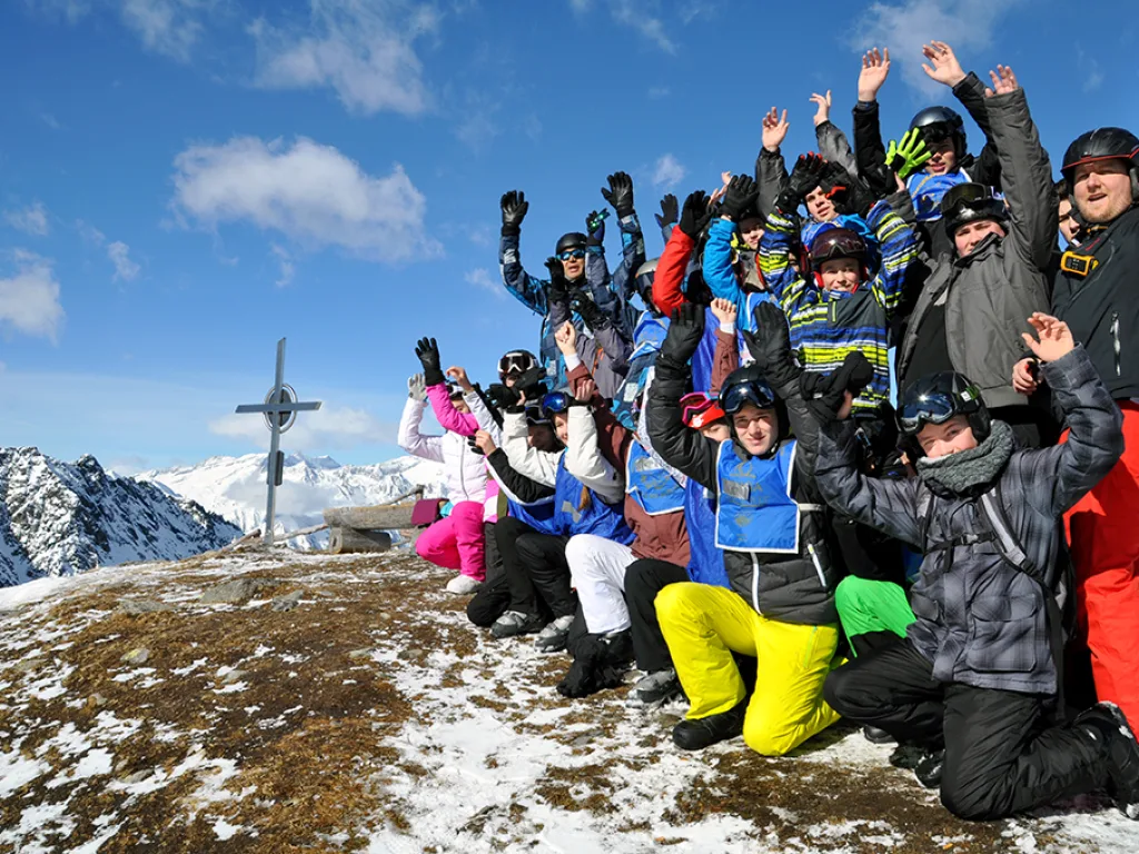 Gruppe jubelt am Gipfelkreuz mit erhobenen Armen.